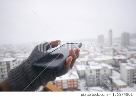 Snowy city view with a hand holding a smartphone Snowy city view with a hand holding a smartphone 135574801