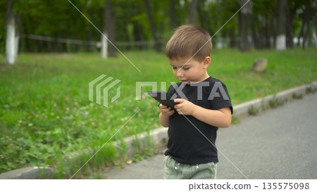 Little boy walking in park looking at smartphone screen 4k 135575098