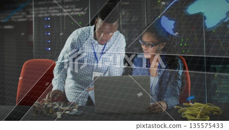 Collaborating lab technicians adjusting circuit boards at tech lab desk, with world map display 135575433
