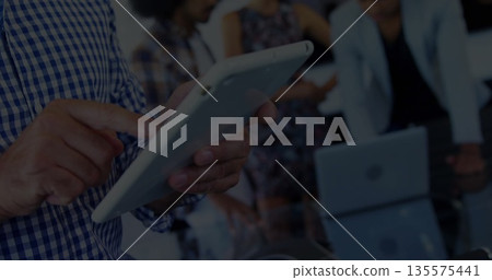 Male wearing blue checkered shirt tapping white tablet in boardroom, with silver laptop, copy space 135575441