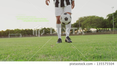 Juggling male soccer player wearing jersey tapping soccer ball mid-air on grass with goalpost view Juggling male soccer player wearing jersey tapping soccer ball mid-air on grass with goalpost view 135575504