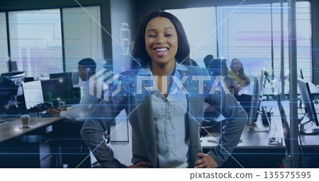 Smiling woman in blue blouse and gray blazer standing in modern office, with holographic panels 135575595