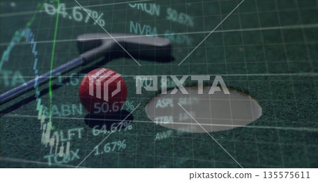 Resting silver putter behind red golf ball near rimmed hole on felt mat, with stock overlay 135575611