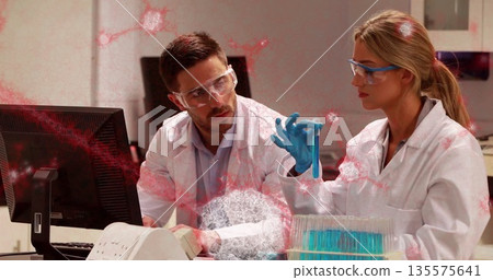 Researchers wearing safety gear examining blue liquid test tube at lab bench, with test tube rack 135575641