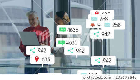 Wearing business attire, two women holding laptop on glass walkway, with floating notifications 135575643