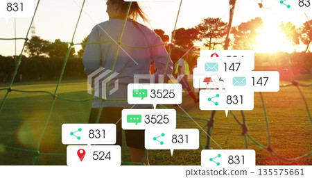 Practicing woman in shorts and sweatshirt on soccer pitch with goal net, bibs and notifications 135575661