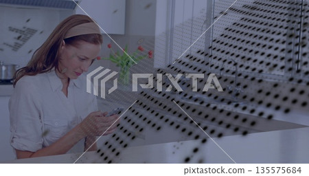 Standing woman wearing shirt checking smartphone at kitchen counter, with tulip vase Standing woman wearing shirt checking smartphone at kitchen counter, with tulip vase 135575684