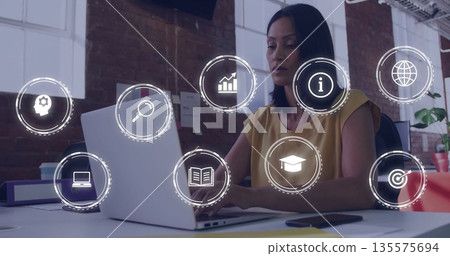 Typing mature woman wearing mustard top at office desk, laptop, digital icons overlay copy space 135575694