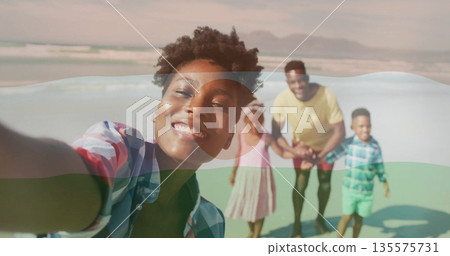 Holding smartphone woman wearing plaid shirt standing on wet sand at beach, with family behind 135575731