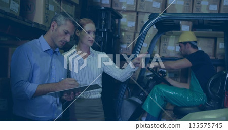 Holding clipboard and pen, two co-workers pointing at inventory in warehouse, with forklift Holding clipboard and pen, two co-workers pointing at inventory in warehouse, with forklift 135575745