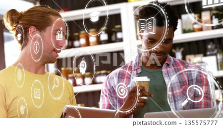 Collaborating coworkers reviewing digital icons at coffee counter with laptops and coffee cup Collaborating coworkers reviewing digital icons at coffee counter with laptops and coffee cup 135575777