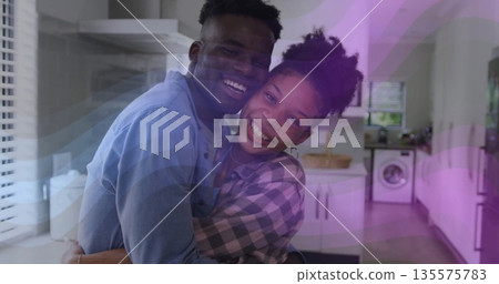 Hugging smiling couple sharing embrace in modern kitchen, with cabinets, washing machine and basket 135575783