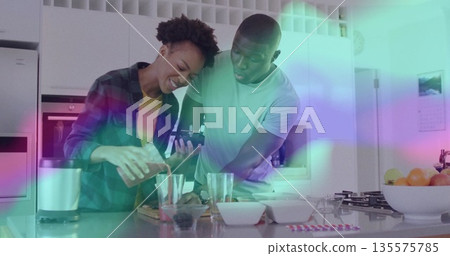 Pouring orange juice cooking couple preparing drink behind kitchen island, with phone and blender Pouring orange juice cooking couple preparing drink behind kitchen island, with phone and blender 135575785