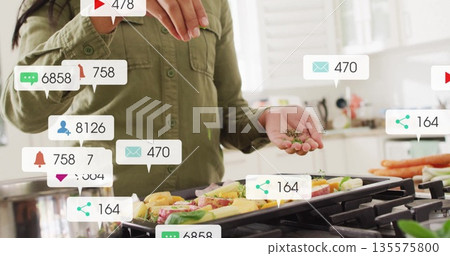 Sprinkling home cook seasoning over veggies on grill pan in home kitchen, with social media icons Sprinkling home cook seasoning over veggies on grill pan in home kitchen, with social media icons 135575800