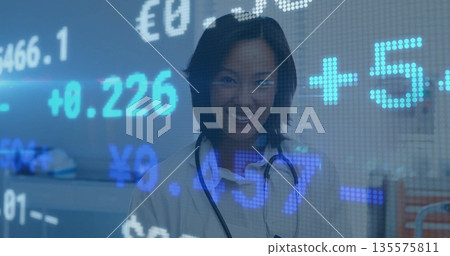 Smiling female doctor reviewing financial overlay in hospital ward, with stethoscope and lab coat 135575811