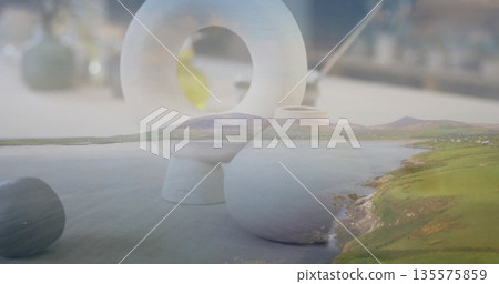 Blending white ceramic sculpture and spherical vase with coastal hills at tabletop double exposure 135575859