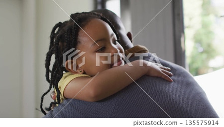 Man hugging child over shoulder and holding securely at home near window, family bond 135575914