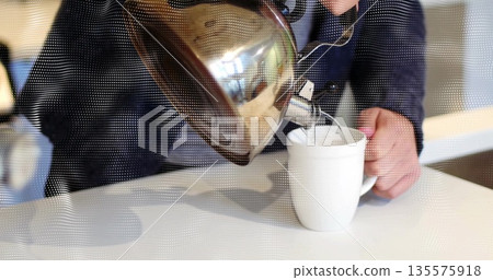 Pouring man wearing dark jacket tilting stainless steel kettle into ceramic mug at cafe counter Pouring man wearing dark jacket tilting stainless steel kettle into ceramic mug at cafe counter 135575918