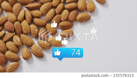 Cluster of almonds on white tabletop, showing thumbs-up icons and notification bubble, copy space 135576323