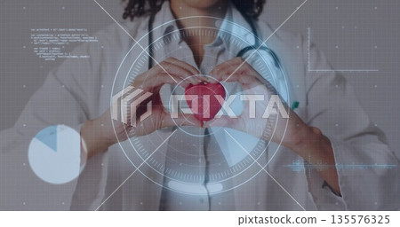 Female physician in lab coat and stethoscope holding heart model at clinic, with digital overlays Female physician in lab coat and stethoscope holding heart model at clinic, with digital overlays 135576325