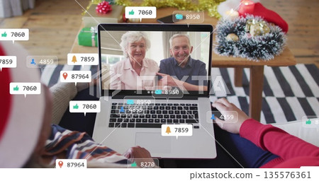Watching senior couple making call on laptop in living room, with holiday wreath, reaction icons 135576361