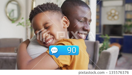 Hugging father and son sharing score moment in modern living room, with blue chat bubble 90 135576376