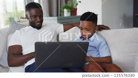 Exploring father and son using black laptop on light colored sofa in living room at home Exploring father and son using black laptop on light colored sofa in living room at home 135576380