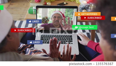 Waving senior and mid-adult women using laptop in decorated living room, with Santa hats and gifts Waving senior and mid-adult women using laptop in decorated living room, with Santa hats and gifts 135576387
