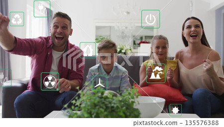 Cheering family raising arms on gray sofa in living room, with floating energy icons Cheering family raising arms on gray sofa in living room, with floating energy icons 135576388