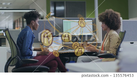 Collaborating pair viewing network graphic at desk behind partition, using laptops dual monitors Collaborating pair viewing network graphic at desk behind partition, using laptops dual monitors 135576453