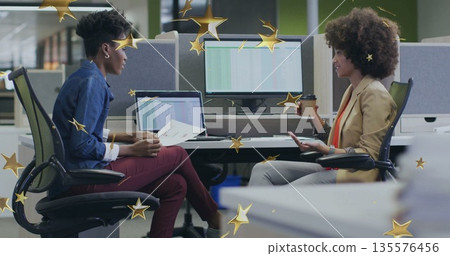 Discussing printed documents, two office professionals sitting at open-plan desk with coffee cup Discussing printed documents, two office professionals sitting at open-plan desk with coffee cup 135576456