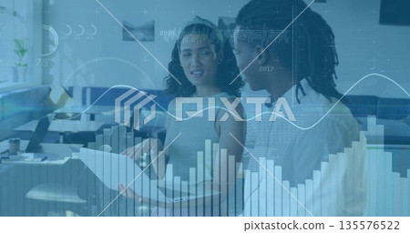 Coworker duo reviewing printed report and laptop in open-plan office, with data overlays Coworker duo reviewing printed report and laptop in open-plan office, with data overlays 135576522