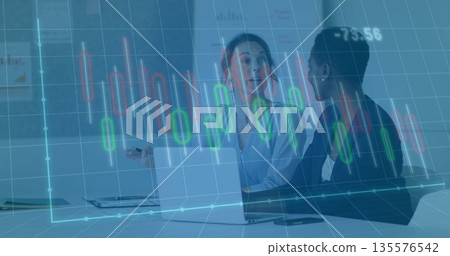 Two women in business attire reviewing candlestick chart at conference table with laptop and charts Two women in business attire reviewing candlestick chart at conference table with laptop and charts 135576542