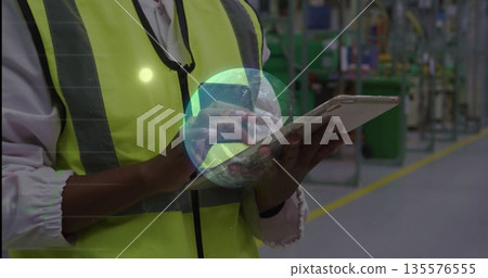 Interacting technician wearing hi-vis vest holding tablet on factory walkway with data overlay Interacting technician wearing hi-vis vest holding tablet on factory walkway with data overlay 135576555