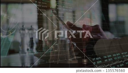 Holding smartphone above laptop keyboard at desk, displaying chart overlays with salt pepper mills Holding smartphone above laptop keyboard at desk, displaying chart overlays with salt pepper mills 135576560