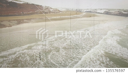 Rolling waves with white foam revealing wet sand on beach, snow-dusted hills, grid overlay hovering 135576597