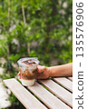 Woman holding iced cappuccino in hand on table outdoors. 135576906