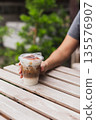 Woman holding iced cappuccino in hand on table outdoors. 135576907