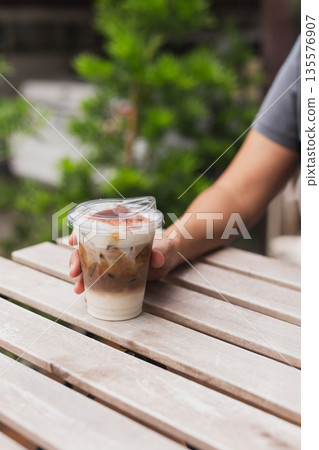 Woman holding iced cappuccino in hand on table outdoors. 135576907