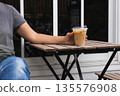 Woman holding iced latte in hand on table outdoors. 135576908