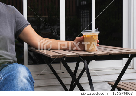 Woman holding iced latte in hand on table outdoors. 135576908