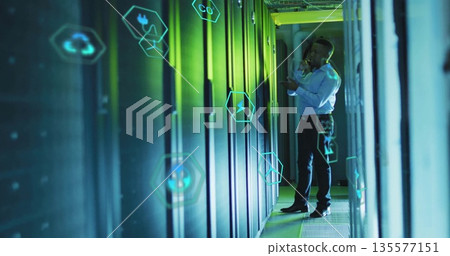 Inspecting technician making phone call in data center aisle, with server racks, icons, copy space 135577151