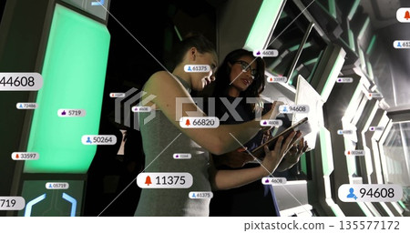 Two female technicians examining floating data icons on tablet in control room, with green panels Two female technicians examining floating data icons on tablet in control room, with green panels 135577172