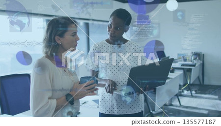 Mid-adult professionals wearing business attire analyzing charts in office with laptop, coffee mug 135577187