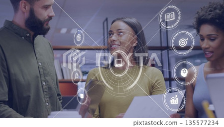 Reviewing printouts and showing tech icons, coworkers wearing casual attire in office using laptop Reviewing printouts and showing tech icons, coworkers wearing casual attire in office using laptop 135577234