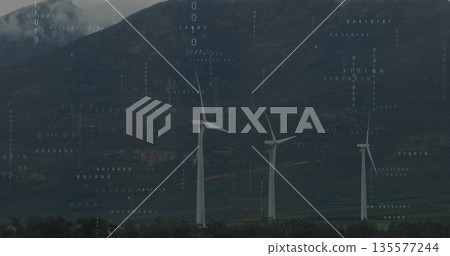 Standing white wind turbines streaming binary code overlay over grassy plain at mountain base Standing white wind turbines streaming binary code overlay over grassy plain at mountain base 135577244