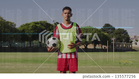 Soccer player wearing fluorescent bib holding black-and-white ball on training field, with goal net 135577256