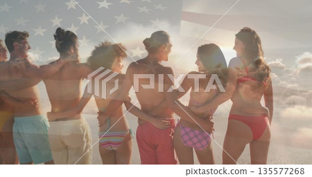 Standing friends wearing swimwear linking arms on beach facing ocean horizon, with US flag overlay Standing friends wearing swimwear linking arms on beach facing ocean horizon, with US flag overlay 135577268