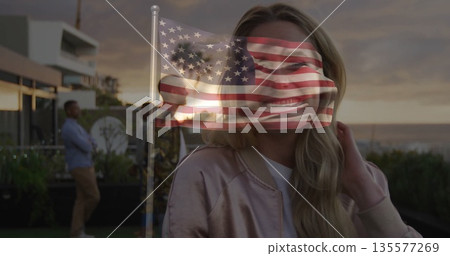 Standing woman in satin jacket overlooking ocean from rooftop, with railing and US flag overlay Standing woman in satin jacket overlooking ocean from rooftop, with railing and US flag overlay 135577269