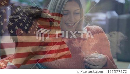 Smiling man, woman in orange sweater sitting on sofa at home, with mug and flag overlay Smiling man, woman in orange sweater sitting on sofa at home, with mug and flag overlay 135577272